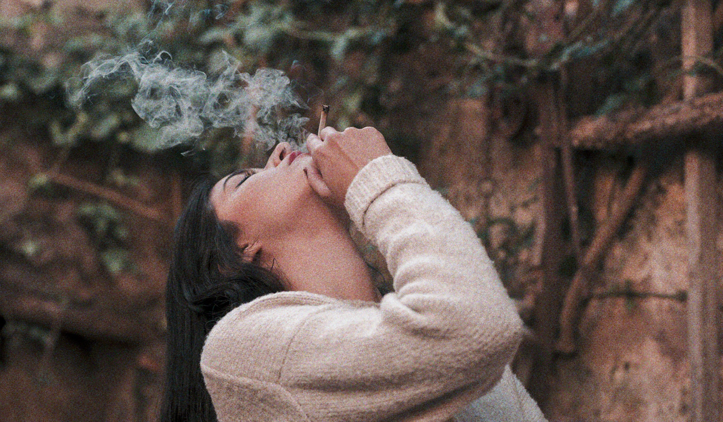 Relaxed vibes: A woman enjoying a cannabis pre-roll in a backyard oasis, surrounded by lush vines.