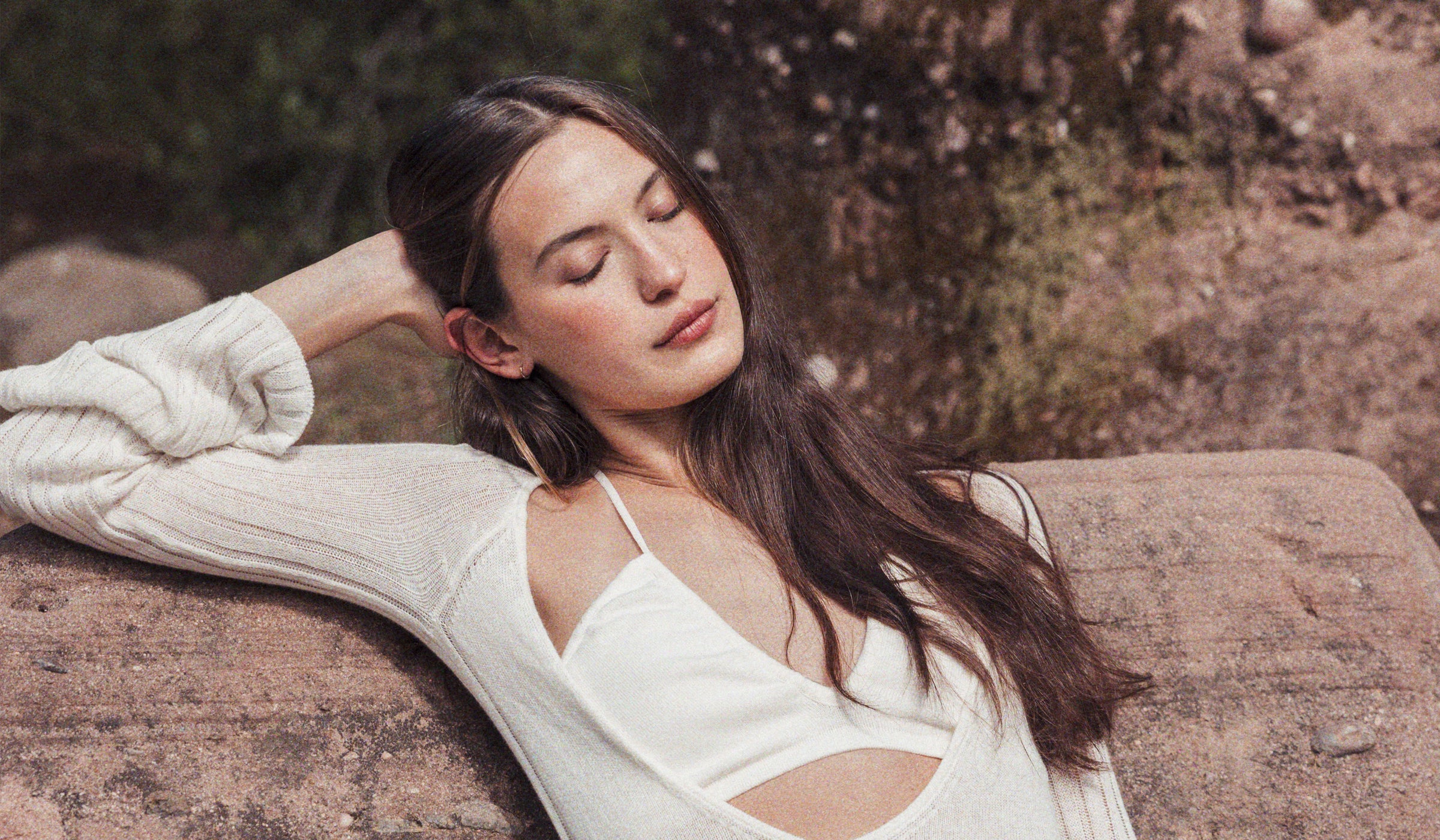 Serenity in nature: A woman with closed eyes, peacefully resting on a large rock amidst the beauty of the outdoors.